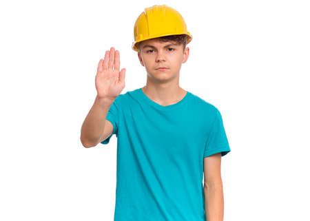 Handsome Teen Boy wearing yellow Hard Hat doing stop sign with palm of hands. Portrait of serious Child making stop gesture and Looking at camera, isolated on white backgroundの写真素材