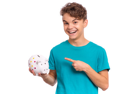 Portrait of teen boy holding Piggy Bank. Cute caucasian young teenager isolated on white background. Saving Money concept. Crazy funny child about to break his piggybankの写真素材