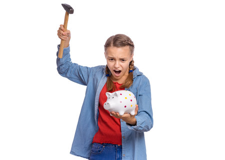 Beautiful teenage girl holds a piggy bank and a hammer in her hands, isolated on white backgroundの写真素材