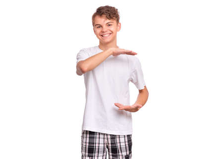 Handsome teen boy shows something in his hands and looking at camera, isolated on white backgroundの写真素材