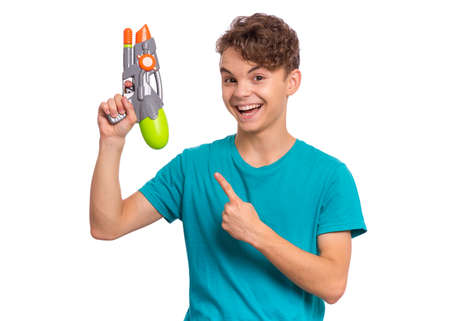 Portrait of happy teen boy playing with plastic water gun, isolated on white background. Beautiful caucasian teenager having fun with children toy. Funny summer games with waterの写真素材