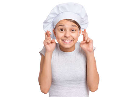 Teen girl in chef hat, keeping fingers crossed and making wish, isolated on white background.の写真素材