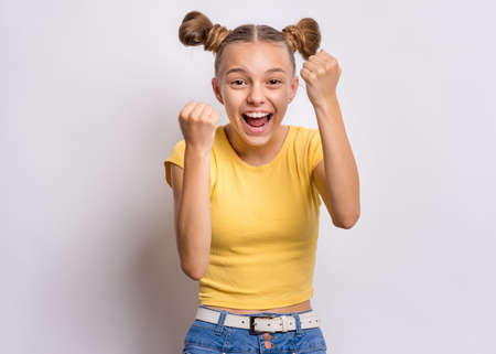 Portrait of teen girl happy and excited expressing winning gesture. Successful and celebrating victory, triumphant child making win sign. Beautiful caucasian teenager, on grey background.の写真素材
