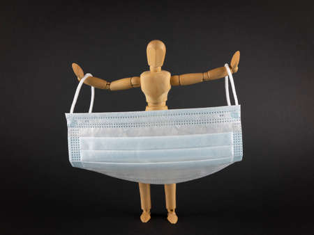 Wooden mannequin holding disposable medical mask on a dark background. Coronavirus prevention...