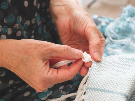 Woman is tying knots to create a fringe on a woven fabric. Finishing of a weave. Concept of handicraft, handworkの写真素材