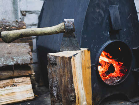 Old ax, firewood and working wood stove with flame of the fire. Lighting the stoveの写真素材