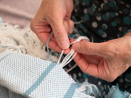 Elderly woman is creating a fringe on a woven shawl. Hands of artisan at work