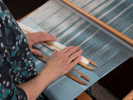 Artisan's hands with two shuttles on the hand loom. Weaving of the fabric with striped patternの写真素材