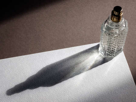 Clear glass bottle of perfume with long and beautiful shadow, copy space