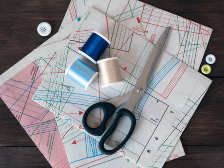 Sheets of pattern for sewing, dressmaking scissors, spools and buttons on a dark wooden background....