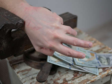 Hands griped in an old vice is reaching for the money. Concept of greed, tax burden, heavy taxesの写真素材