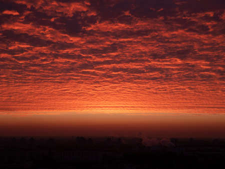 Red ominous clouds hovering above the ground at dawn. Red-tinted sky at sunrise. Landscape of tonal reds in the early hoursの写真素材