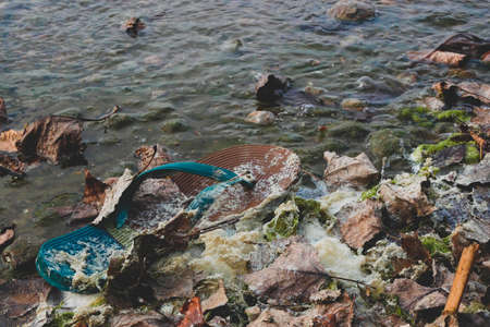 Floating unattended flip-flop, foliage and dirty foam in the water on the beach. Concept of water...