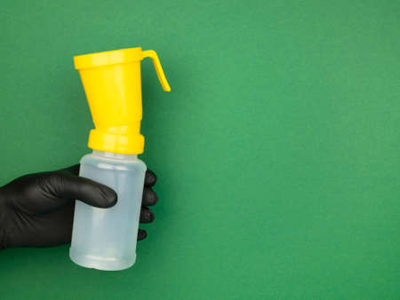 Hand in black nitrile glove holds a teat dip cup for udder cow disinfection on the green background, copy space. Milking procedureの写真素材