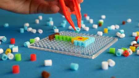Arranging colorful cylindrical beads on the transparent frame with tweezers, selective focus....