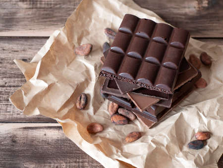 Chocolate bars and cocoa beans on the rustic background. Chopped pieces of dark and milk chocolate...