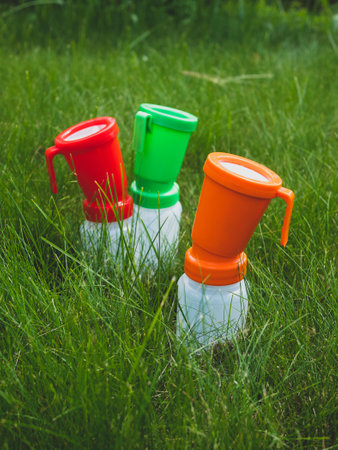 Three colored teat dip cups for cattle on the grass, selective focus. Concept of hygiene and disinfection of cow's udder. Health care of udder before and after milkingの写真素材