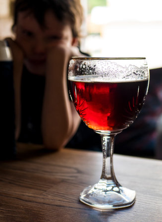 Beer glass and a sad child on the background, selective focus. Parental problem drinking. Underage drinkingの写真素材
