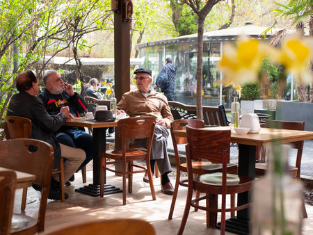 Yerevan, Armenia - 27 March 2023: Senior friends in a cozy outdoor cafe are drinking coffee, smoking and talking about life, selective focusのeditorial素材