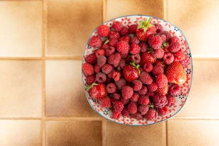 Plate of fresh strawberries and raspberries in a kitchen top view