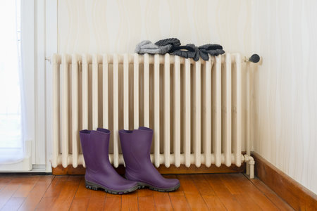 Boots, hat and gloves drying on a cast-iron radiatorの写真素材