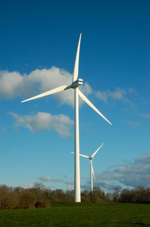 Vertical view of two wind turbines against a blue sky with a few cumulus clouds