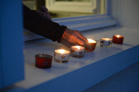 An elderly woman's hand lighting small candles on a windowsill at nightfall for the Festival of Lights.の写真素材