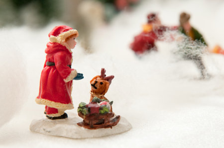 A miniature village scene in fake snow, with the foreground focused on a child dressed as Santa Claus and a small dog.の写真素材