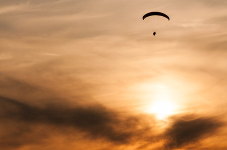 Small silhouette of a paramotor in flight at sunsetの写真素材