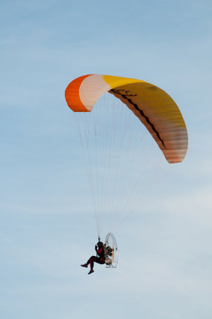 Paramotor flight with a yellow wing against a blue skyの写真素材