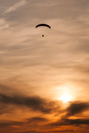 Vertical view of a small silhouette of a paramotor in flight at sunsetの写真素材