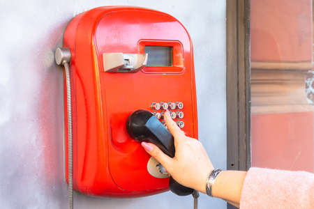 a woman's hand dials a phone number on a public pay phone.の写真素材