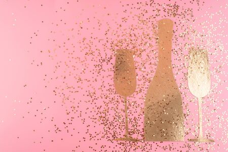 Champagne bottle and two glasses carved from decorative cardboard  surrounded by gold confetti stars on a pink pastel background. Top view. Christmas card blank. Copy space and horizontal orientation.の写真素材