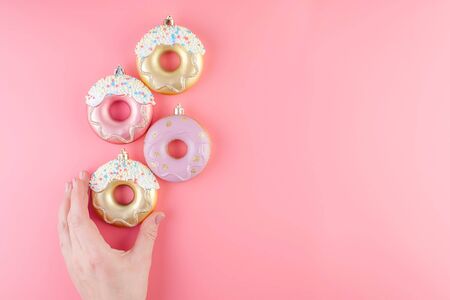 Female hand holds New Year donut-shaped Christmas tree toys on a pink pastel background. Top view. Card blank. Copy space and horizontal orientation.の写真素材
