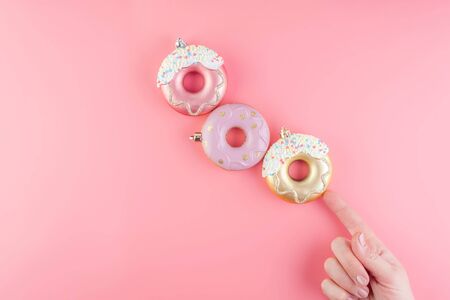 Female hand holds New Year donut-shaped Christmas tree toys on a pink pastel background. Top view....