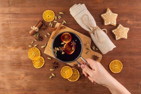 Mulled wine. A home-made organic red wine hot drink. Rustic Christmas decoration on wooden background, natural fabric, with oranges and cinnamon. Hand holds prepared drink.
の写真素材
