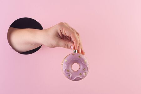 Hand holds a donut christmas ball through a hole in paper pink background. Template for design. Copy space and horizontal orientation.の写真素材