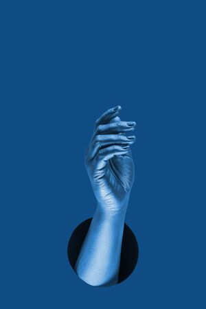 Hand shows  different gestures and symbols from the hole on a blue paper background. Template for design. Trend color of 2020 concept. The color of the year. Classic deep blue. の写真素材