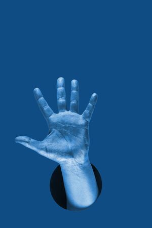 Hand shows  different gestures and symbols from the hole on a blue paper background. Template for design. Trend color of 2020 concept. The color of the year. Classic deep blue.の写真素材