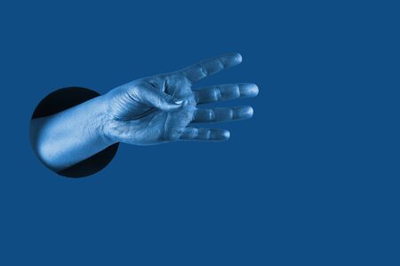 Hand shows  different gestures and symbols from the hole on a blue paper background. Template for design. Trend color of 2020 concept. The color of the year. Classic deep blue. の写真素材