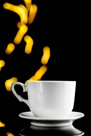 White cup with beautiful bokeh on a black background. Design concept. Copy space. Close up and vertical orientation.の写真素材