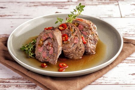 Beef tenderloin rolls stuffed. Slices of meat served on a plate in a sauce and with fresh vegetables and herbs. Close up and horizontal orientation. の写真素材