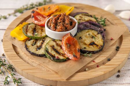 Grilled vegetables with fresh spicy greens and pesto sauce of red tomatoes. Garnish for ketogenic and paleo diets. Large portion on a wooden plate in a rustic style. Close up and horizontal orientation.  Selective focus.
の写真素材