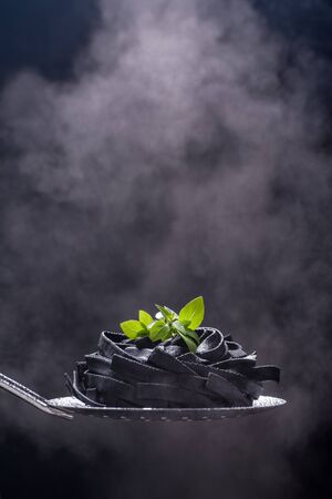 Fettuccine homemade uncooked pasta. Dark color of the product on a black background. Portion on the ladle is ready for cooking. Steam from hot product. Close up. Copy space. Vertical orientation.の写真素材