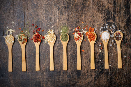 Various spices in wooden spoons on a dark brown background. Assorted condiments for cooking. Top...