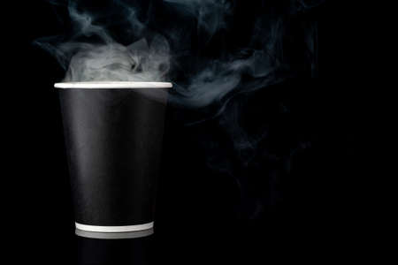 Black cup of coffee with a white cap on a black background. Hot drink with steam. Recycled and recyclable coffee paper cup. Copy space and horizontal orientation.の写真素材