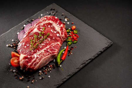 Raw uncooked beef steak. A large piece of meat on the bone lies on a wooden board with spices and...