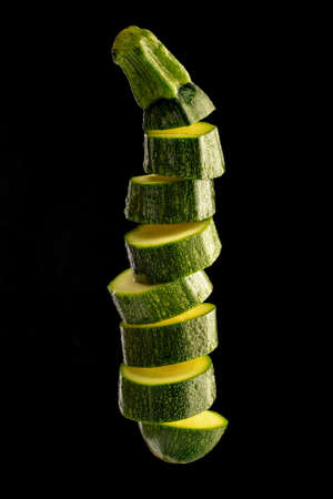 Ripe zucchini cut into slices and tossed into the air isolated on black background. Food levitation. Creative concept with food.の写真素材