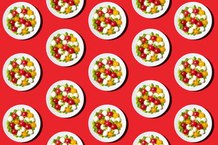 Fresh salad with cherry tomatoes, mozzarella cheese and microgreens. Pattern from a plate on a red background. Top view. Creative food concept.の写真素材