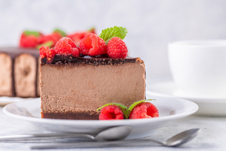Chocolate cheesecake with fresh raspberries and mint leaves. A piece of cake is cut and served on a plate. Homemade dessert. Close-up.の写真素材